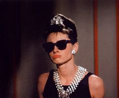 a woman wearing sunglasses and pearls in a black dress