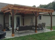 a covered patio with chairs and tables in front of a house that has a grill on it