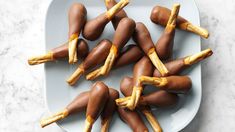 chocolate covered hotdogs are arranged on a white platter with golden sticks sticking out of them