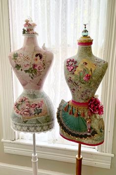 two mannequins are sitting on display in front of a window with white curtains