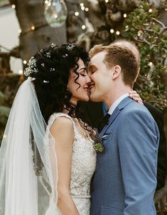 a bride and groom kissing in front of a tree with lights on it's branches