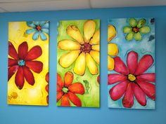 three brightly colored paintings hang on the wall in an office space with blue walls and flooring