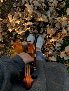 a person holding a violin in their hand while sitting on the ground with leaves around them