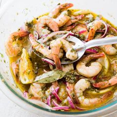 a glass bowl filled with shrimp and vegetables next to a silver serving utensil