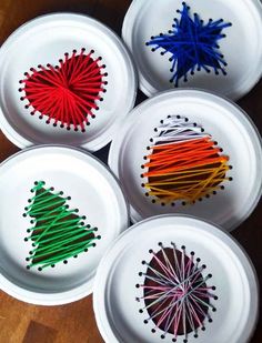 four paper plates with different colored string art designs on them, sitting on a wooden table