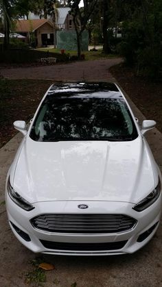 a white car parked on the side of a road next to a tree filled street