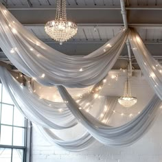 a chandelier hanging from the ceiling in a room with white drapes and lights