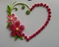 a heart shaped object made out of paper with flowers and leaves on the side, sitting on a white surface