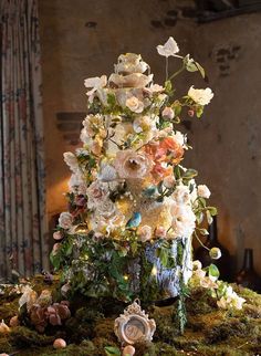 an elaborately decorated christmas tree in the middle of a moss covered table with flowers on it