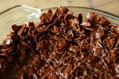 a glass bowl filled with chocolate granola on top of a wooden table next to a knife