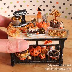 a hand is holding a miniature table with food on it and pumpkins in the background