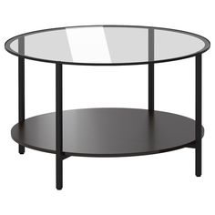 a round glass table with black legs and a shelf on the bottom that holds an object