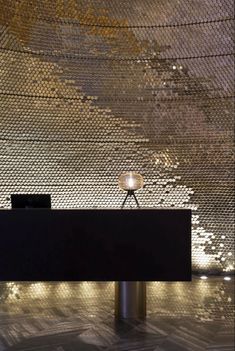 a desk with a lamp on top of it in front of a wall covered in gold and silver sequins