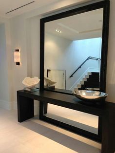 a large mirror sitting on top of a wooden table next to a bowl and vase