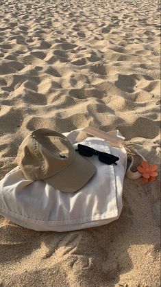 a hat and sunglasses laying on top of a bag in the sand at the beach