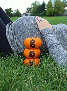 a woman laying in the grass with her hands on top of two orange pumpkins