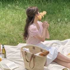 a woman sitting on a blanket eating food and drinking wine while holding a baguette