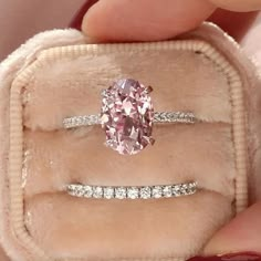 a pink diamond ring sitting on top of a velvet case in someone's hand