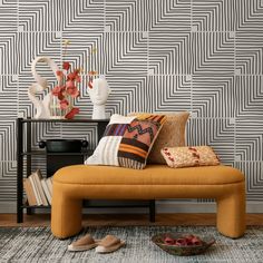 a yellow bench with pillows on it in front of a wallpapered background and vases