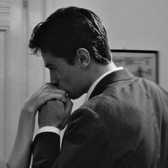 a black and white photo of a man in a suit looking down at his tie