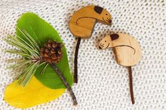 two wooden animals are sitting next to each other on a white surface with green leaves and pine cones