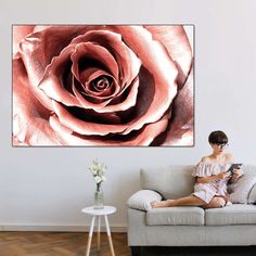 a woman sitting on a couch in front of a wall with a large pink rose