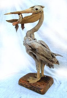 a statue of a pelican holding a fish in its beak on top of a piece of driftwood