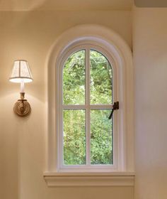 a white toilet sitting under a window next to a wall mounted light and a lamp