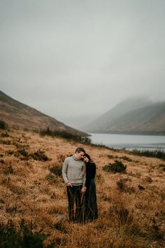 an engaged couple standing in the middle of a field with mountains in the back ground