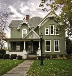 a green house with white trim on the front and side windows, along with a black lamp post