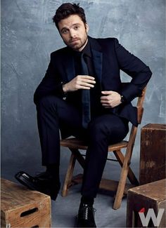 a man in a suit and tie sitting on a wooden chair with his hands on his hips