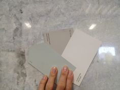 a person's hand holding some paint swatches on a marble counter top with white and gray colors