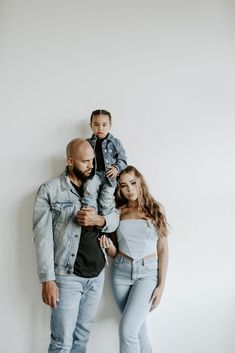 a man, woman and child are standing in front of a white wall with their arms around each other