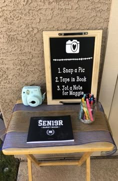 a small table with a sign on it and some pens, pencils, and a camera