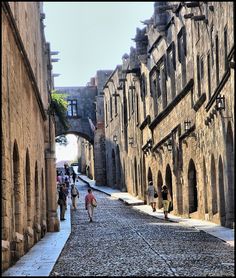 people are walking down an alleyway between two buildings with stone walls and arched doorways