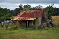 an old rusted out building in the middle of a field with trees and grass