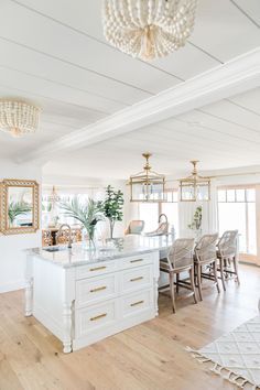 a white kitchen with an island in the middle and lots of chairs around it on top of hard wood flooring