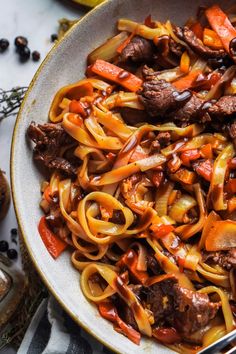 a bowl filled with beef and noodles on top of a table next to utensils