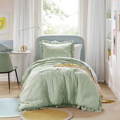 a bed with green comforter and pillows in a room next to a window,