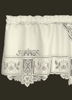 a white window valance with flowers and lace on the bottom, hanging from a black wall