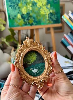 a woman holding up a gold frame with a painting in the background