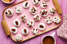 cupcakes with white frosting and pecans are on a pink tray next to a cup of coffee