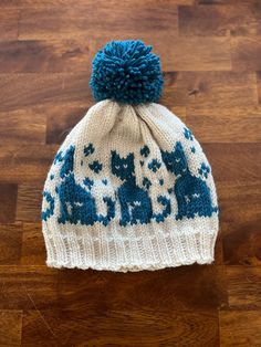 a blue and white knitted hat with animals on it sitting on a wooden floor