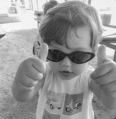 a little boy wearing sunglasses giving the thumbs up sign with his thumb in black and white