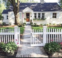 a white picket fence in front of a house with trees and flowers on the sidewalk