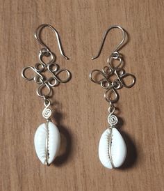 two white seashells hanging from silver earwires on a wooden table top