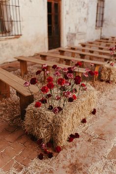 several wooden benches with flowers growing out of them on hay bales in front of an old building