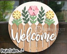 a welcome sign hanging from the side of a wooden door with flowers and leaves on it