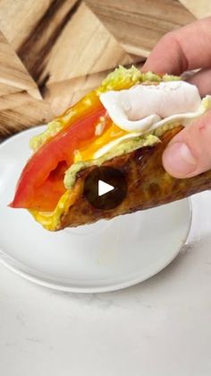 a person is holding an egg and tomato burrito on a white plate with a wooden table in the background