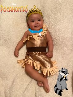 a baby wearing a gold dress with a crown on it's head and holding a raccoon toy